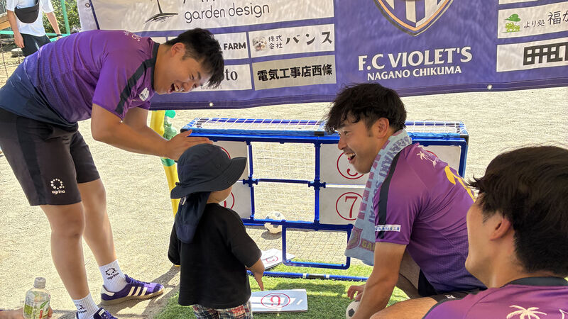 イベント会場のシュートゲームで、選手たちが子どもと笑顔で交流している様子。